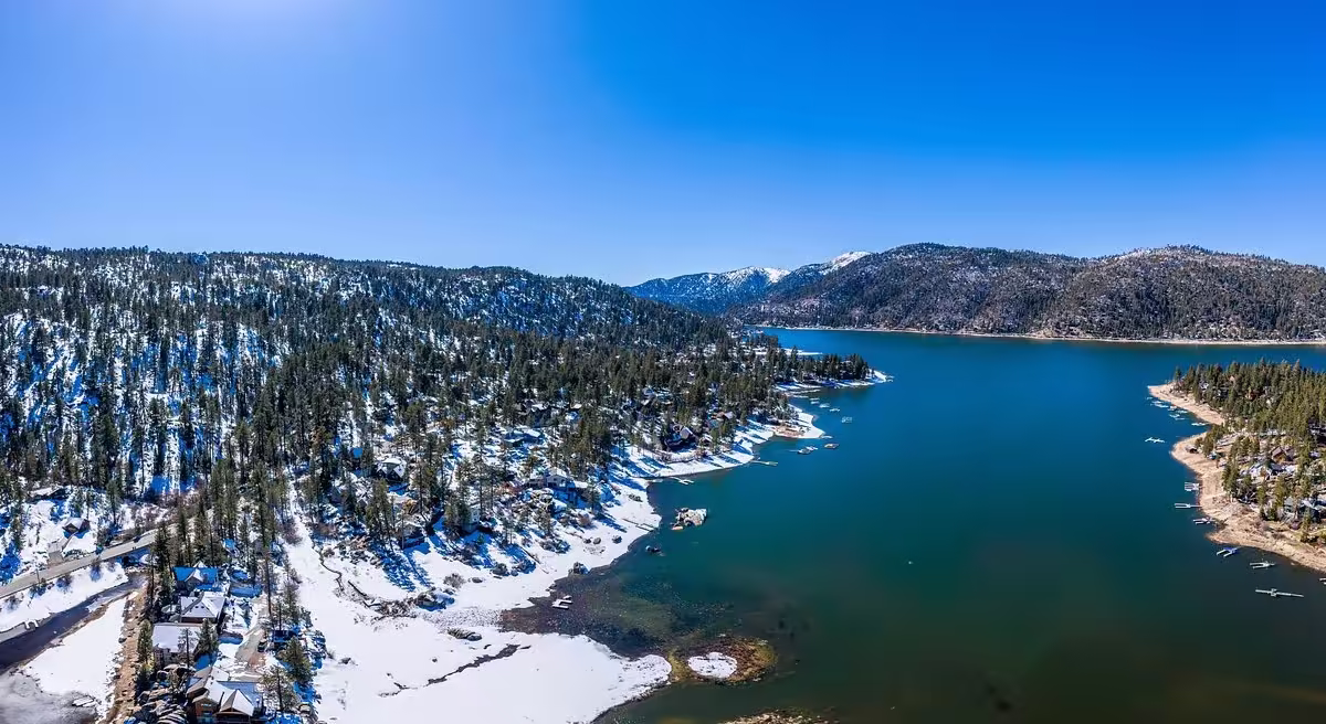 Big Bear Lake Aerial view of a mountain lake surrounded by snow-covered forest and lakeside cabins in winter